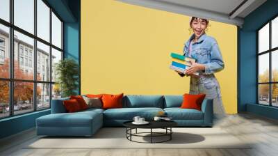 Happy Asian girl holding book and jumping over yellow background. back to school concept. Wall mural