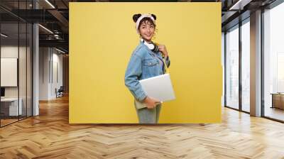 Happy Asian girl student with laptop and backpack isolated on yellow studio background. Wall mural