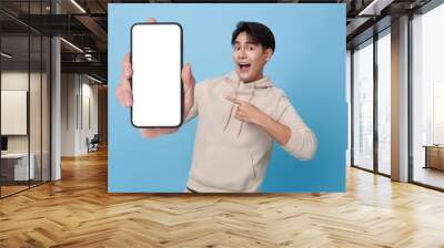 Happy Asian man showing and pointing finger to smartphone mockup of blank screen isolated on blue background. Wall mural