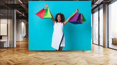 Happy beautiful african woman in white dress and hand holding shopping bag isolated over blue background. Wall mural