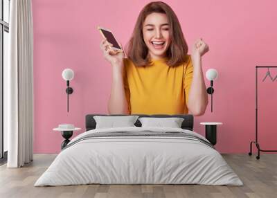 happy young woman celebrating with mobile phone isolated over pink background. Wall mural