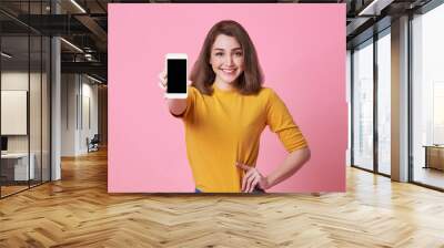 Portrait of happy young woman showing at blank screen mobile phone isolated over pink background. Wall mural