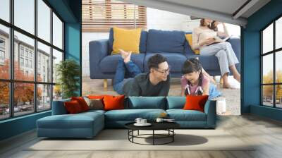 Relax Asian mother reading a book on sofa and father with daughter using tablet in living room at home. Wall mural