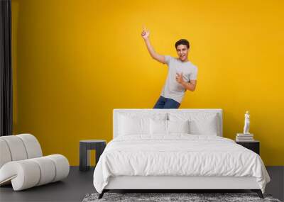 smiling handsome Asian man pointing fingers to empty space aside isolated on yellow studio background. Wall mural