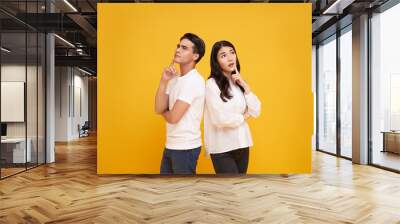 young asian man and woman thinking and touching chin while looking aside isolated on yellow background. Wall mural