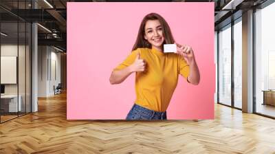 Young smiling beautiful woman in yellow shirt showing credit card in hand over pink background. Wall mural