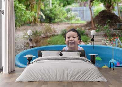 Asian cute child boy laughing while playing water in blue bowl with relaxing face and wet hair in rural nature. Young kid having happy moment in summer. Family activity at home and preschool concept. Wall mural