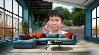 Asian cute child boy show victory sign or two finger with smiling face outdoor. Concept of success, winner, positive thinking, Wall mural