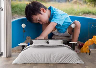 Asian little child boy playing car toy and sand in sandbox outdoor with happy face in natural background. Young kid in blue t-shirt in family relax and freedom time in summer holiday. Wall mural