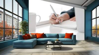 Cropped shot of female hand using pen writing on blank notebook while sitting at office desk. Wall mural