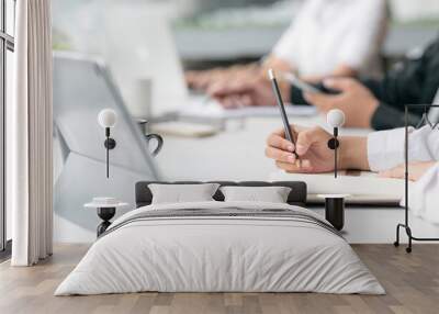 Cropped shot of woman hand writing on notebook with pencil while sitting with her teamwork at office. Wall mural