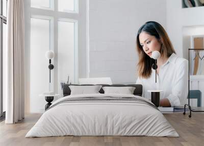 Portrait of young businesswoman looking at laptop screen while sitting at office desk in modern office. Wall mural