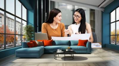 Two asian business women sit at desk discuss project details, share opinion, working on collaborative task Wall mural