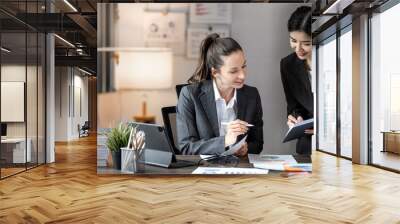 Two businesswoman pointing to graphs and charts to analyze market data,  net profit to plan new sales strategy to increase production capacity. Wall mural