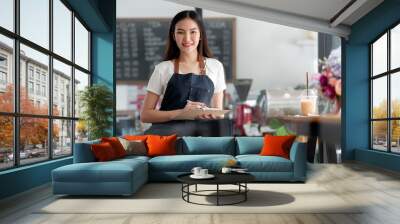 Young beautiful entrepreneur working at her coffee shop, serving for her customer. Wall mural