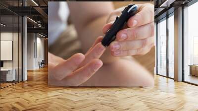 Medicine, diabetes, glycemia, healthcare and people concept - close up of a man's hands using a lancet on his finger to check blood glucose meter with copy space for text Wall mural