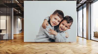 Photo of two adorable boys brothers or friends embracing and smiling joyfully on a gray background. Wall mural