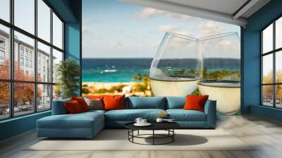 Wide image with a close-up of two clinking glasses of white wine outdoor. Sea and island background at the port of Nassau in the Bahamas. Wall mural