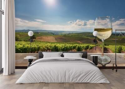  A wine glass of white wine placed on the edge of a terrace overlooking a vineyard. The viney Wall mural