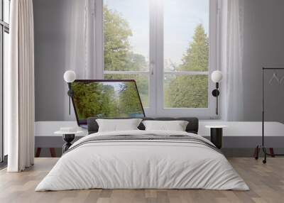 A clean, white desk with a single laptop open, facing towards a window with soft natural lig  Wall mural