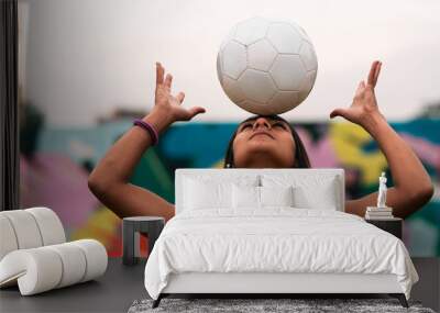 View of a beautiful brunette female soccer player posing, holding and fooling around with a soccer ball. Standing on a green grass outdoors, with a colorful background. Sportswear. Sports and wellness Wall mural