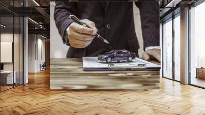 A businessman in a formal suit signs a contract, hands close up, highlighting financial terms like amortization, APR, and asset management, documents symbolizing various loan and insurance concepts. Wall mural