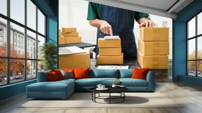 A man is working at his desk, preparing parcel boxes for shipment. He checks and packs items carefully, using shockproof materials, and attaches labels before sending them to customers via EMS. Wall mural