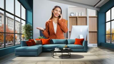 An Asian businesswoman sits at a table, working with a smile. She manages her online Kuya business with enthusiasm, showcasing her dedication and positive attitude while handling tasks efficiently. Wall mural