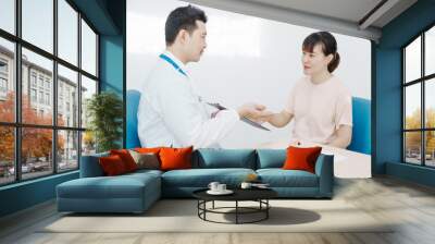 Asian female doctor listens to belly of pregnant mother during a prenatal exam in clinic. doctor provides caring advice, ensuring the health and happiness of the expecting mother and baby. Wall mural