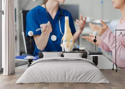 Caucasian female doctor explain to asian female patient using knee bone model at desk in medical room, medical learn aid anatomy instrume, Knee Osteoarthritis, loose patella Wall mural