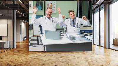 Caucasian middle-aged male doctor and Italian scientific researcher are seated at desk, discussing innovative antiviral drug inventions, with a monitor displaying the latest technology advancements. Wall mural