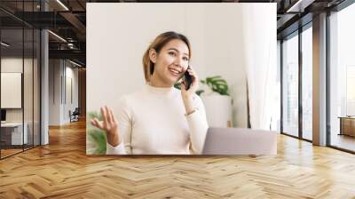 Happy asian businesswoman sitting at desk talking with mobile phone with somebody in office workplace. Wall mural