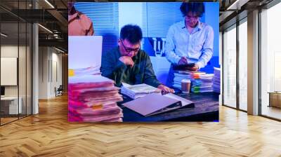 Three men work overtime at night, stressed and overloaded with tasks. They are exhausted, checking documents, and discussing plans. Despite their efforts, they struggle to complete the work on time Wall mural