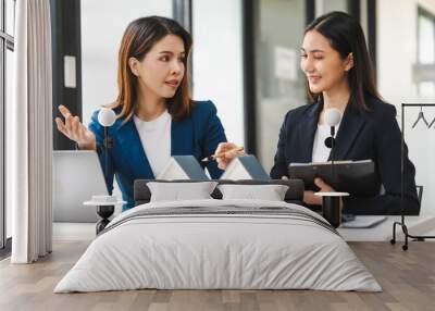 Two Asian real estate agents in formal suits discuss a contract with house models on the table, ready to sign a deal. Wall mural