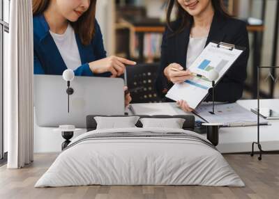 Two middle aged and young Asian female executives in formal suits review bar chart, discussing business strategies in office setting, senior executives or directors in advertising or public relations Wall mural