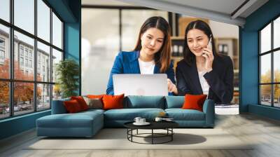 Two middle aged and young Asian female executives in formal suits review bar chart, discussing business strategies in office setting, senior executives or directors in advertising or public relations Wall mural