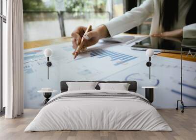 A businesswoman sits at her desk, calculating financial data on her laptop. Surrounded by paperwork and charts, she analyzes expenses and income, reflecting her role in corporate finance and accountin Wall mural