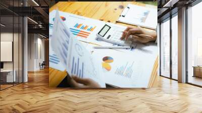 A businesswoman sits at her desk, calculating financial data on her laptop. Surrounded by paperwork and charts, she analyzes expenses and income, reflecting her role in corporate finance and accountin Wall mural