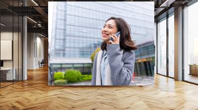 Young beautiful girl walking outside office building using mobile phone and happily calling customers Wall mural