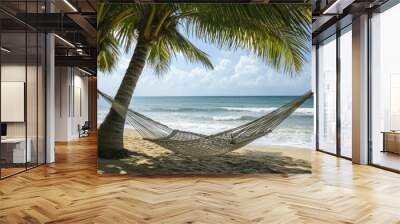 A hammock tied between two palm trees on a beach, gently swaying in the breeze with ocean waves in the background. Wall mural