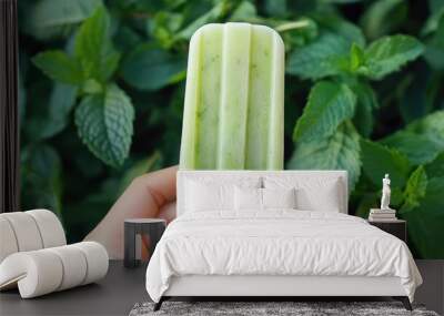 A hand holding a refreshing mint popsicle, with fresh mint leaves scattered in the background. Wall mural