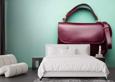 A lady's messenger bag in deep burgundy leather with a sleek design, isolated on a pastel green background Wall mural