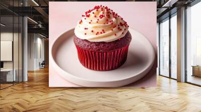 A red velvet cupcake topped with cream cheese frosting and red sprinkles, placed on a white plate against a soft pastel background Wall mural