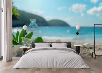 Plastic water bottle on a sandy beach with seashells and greenery. Wall mural