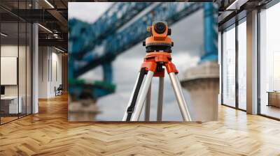 optical level on a cloudy day against the background of huge crane construction.Surveyor's work tool against the background of the construction site. Measuring tool of the geodetic service. Wall mural