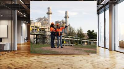 Two brilliant female engineers engaged in a dynamic discussion at a bustling refinery plant in the heart of the industry. Embracing diversity and driving innovation in engineering. Wall mural