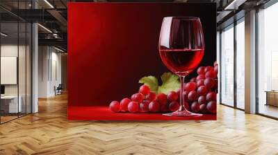 A beautiful glass of red wine beside fresh grapes on a vibrant red background, perfect for beverage or culinary themes. Wall mural