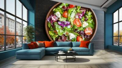 A vibrant salad filled with fresh greens, cherry tomatoes, and colorful vegetables served in a rustic bowl on a dark surface. Wall mural