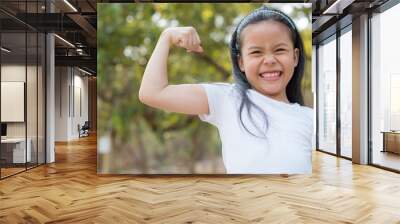 happy Little asian girl child standing showing front teeth with big smile.  showing arms muscles smiling proud. Looking camera showing biceps. fresh healthy green bio background. Fitness concept. Wall mural