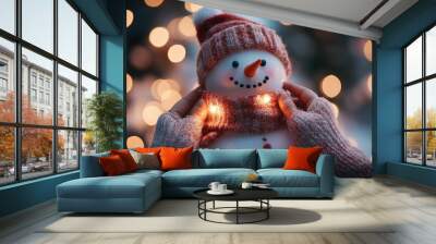 Two hands adjusting a Christmas scarf on a snowman, bright festive lights glowing with holiday cheer in the background. Wall mural